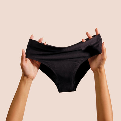 Black Diva reusable period underwear held by hands against a beige background